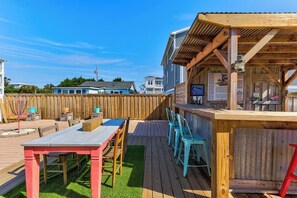 Una terraza de madera con una mesa y sillas, un área de estar cubierta y un patio trasero cercado.