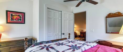 Une chambre à coucher comprenant un lit, une commode, un ventilateur de plafond et une porte donnant sur une autre pièce.