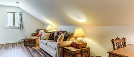 A loft-style room with a sofa, two lamps, a wooden chest, and a dining table.