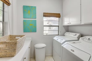 Une buanderie équipée d’un lave-linge, d’un sèche-linge, d’une poubelle et de deux œuvres d’art accrochées au mur.