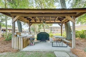 Un espace barbecue extérieur abrité, équipé d’un gril, d’un évier et d’une table de pique-nique.