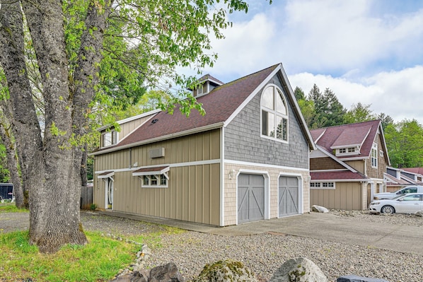 A two-story house with a garage, a large tree in the front yard, and a gravel driveway.