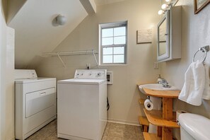 A compact laundry area with a washing machine and dryer, a wooden vanity with a sink, and a window providing natural light. - Near Oregon Caves: 2-studio Retreat w/ Game Room! (Cave Junction)