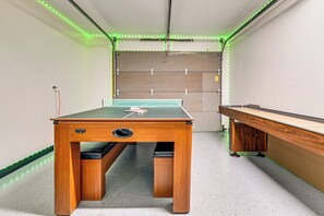 A pool table with a green felt surface, a wooden table with a drawer, and LED strip lighting along the ceiling.