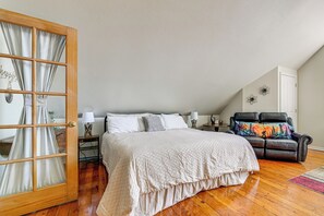 A bedroom with a large bed, a wooden door with curtains, a leather sofa, and a small table with a lamp.