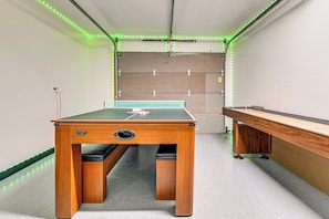 A pool table with a green felt surface, a wooden table with a black felt top, and LED strip lighting along the ceiling.