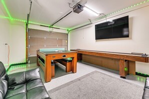 A room with a pool table, leather chairs, a projector, and green LED lights.