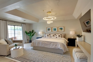 A modern bedroom with a bed, a sofa, a round coffee table, and a large plant.