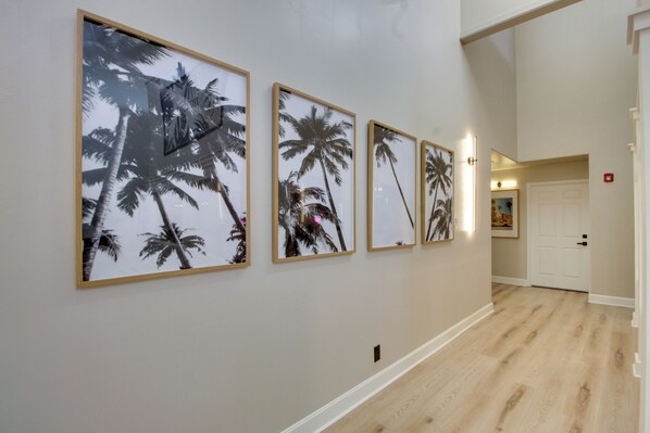 A hallway with framed artwork of palm trees, a wooden floor, and a door at the end. - Boutique Stay Near Louisburg Wedding Venues (Louisburg)