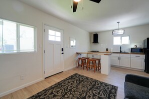 A modern kitchen with white cabinets, a central island with stools, a black range hood, and a hanging light fixture. - Pet-friendly Phoenix Retreat: Main House + Casita! (Phoenix)