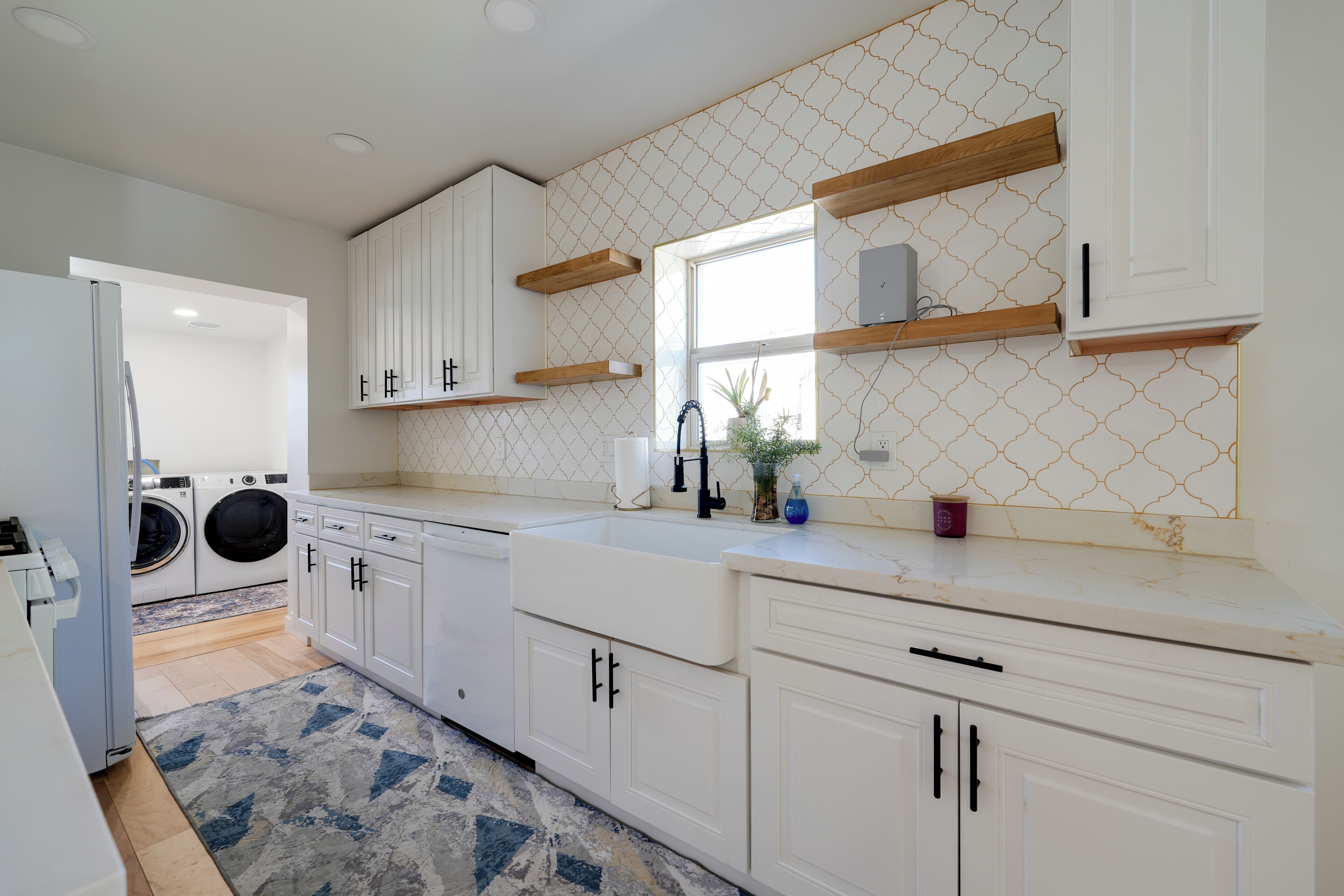 A modern kitchen with white cabinetry, wooden shelves, a built-in washing machine, and a patterned backsplash.