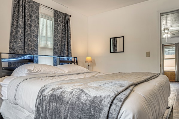 Une chambre à coucher avec un lit, une table de chevet, une lampe, une fenêtre avec des rideaux et une porte.