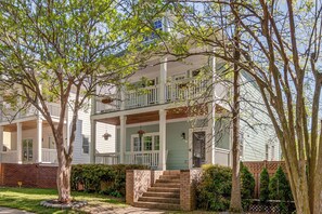 A two-story building with a front porch, a brick staircase, and a small garden area.