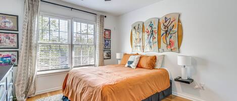 A bedroom with a bed, window, ceiling fan, artwork, and a bedside table.