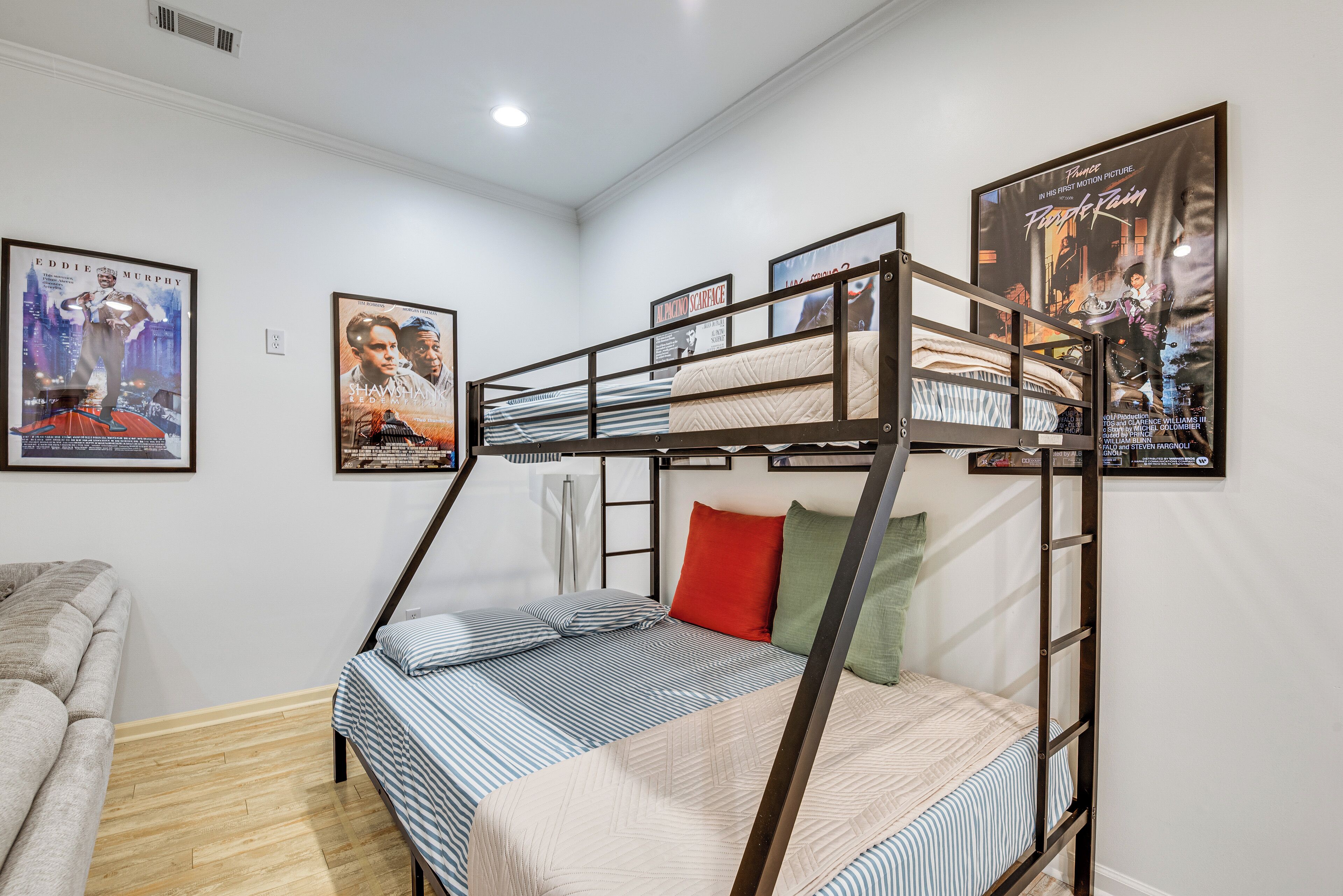 Una cama litera con escalera, una cama individual y un sofá. Hay carteles en las paredes.