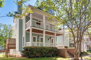 A two-story building with a porch, a brick wall, and a tree.