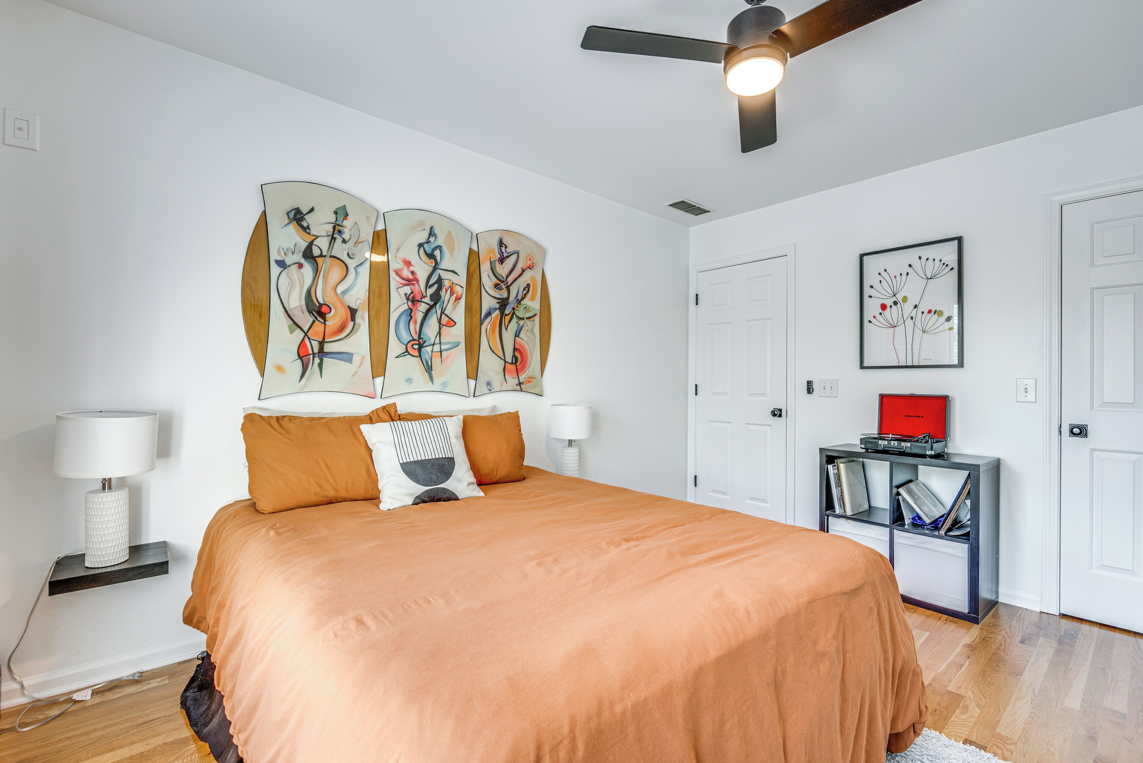 Un dormitorio con una cama, un ventilador de techo, una estantería y obras de arte en las paredes.