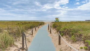 A pathway leading to a beach with a lifeguard tower, surrounded by sand and vegetation. - Elegant Waterfront Condo w/ Views in Pompano Beach (Pompano Beach)