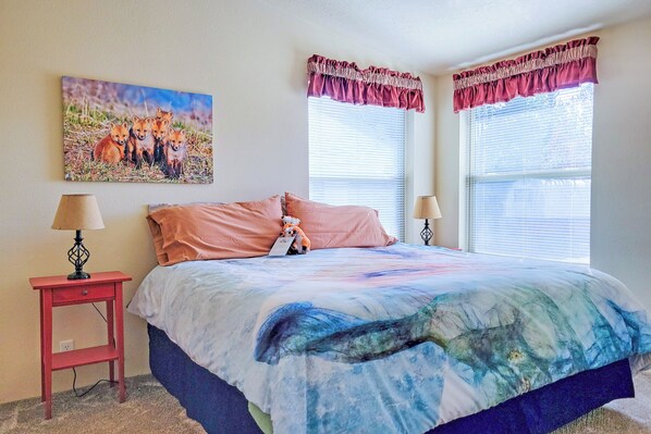 A bedroom with a bed, two bedside tables, a wall-mounted lamp, a window with blinds, and a painting of foxes. - 'fox Cabin' - 6 Blocks to Yellowstone Nat'l Park! (West Yellowstone)