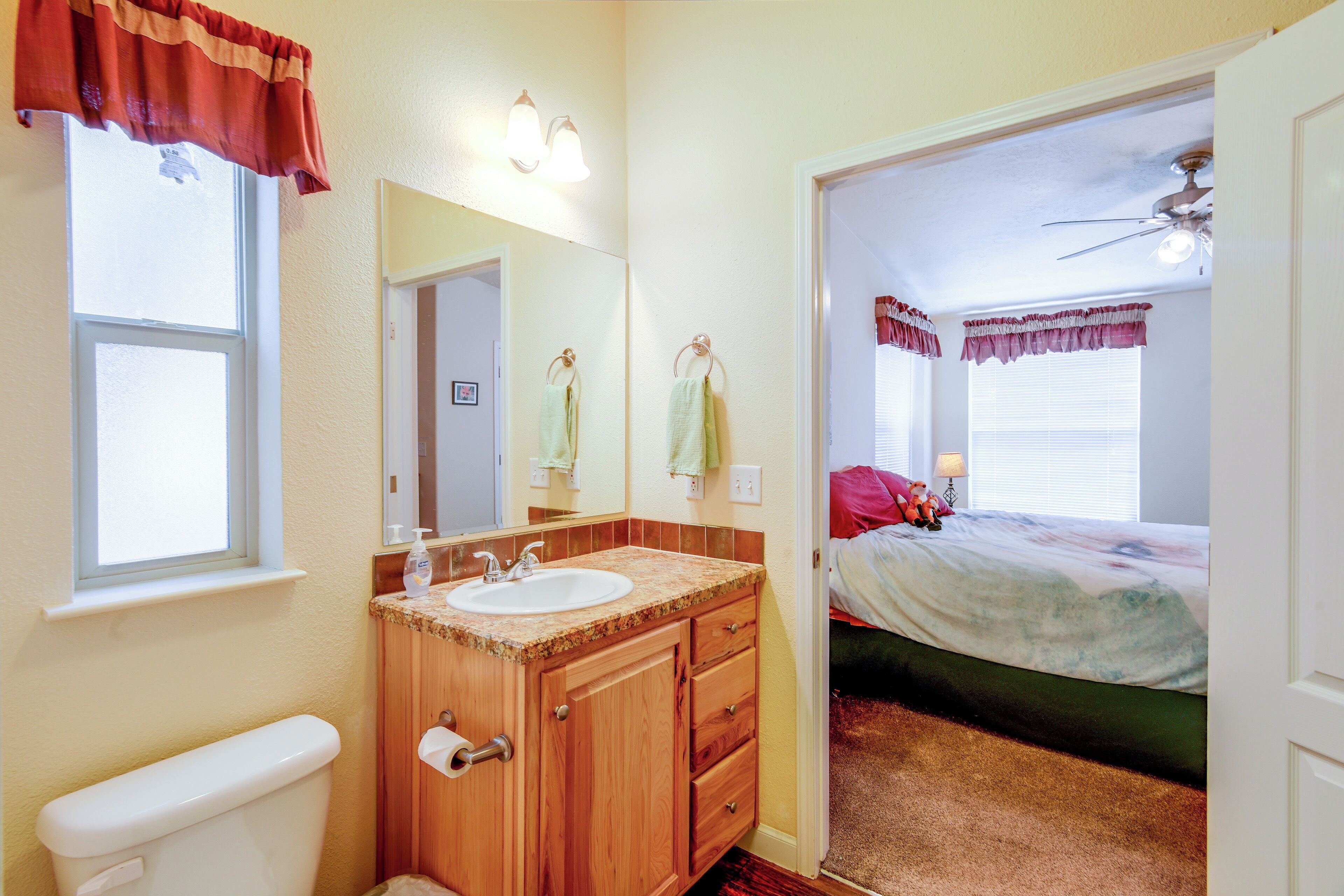 A bathroom with a toilet, sink, and vanity, and a bedroom with a bed and a ceiling fan.