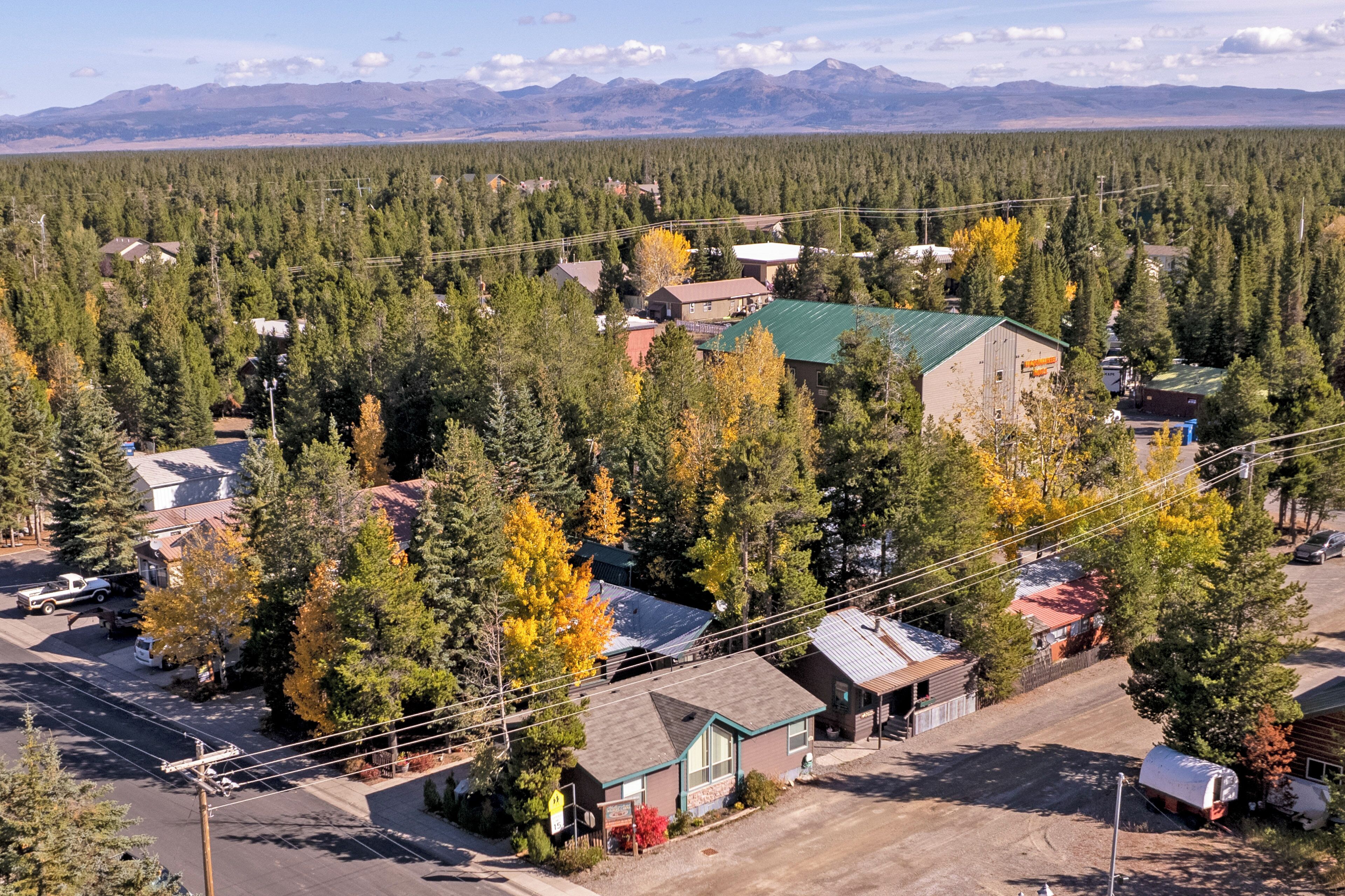 Un quartier résidentiel où les maisons sont entourées d’une forêt dense, avec une route dégagée et des montagnes qui se dessinent à l’horizon.