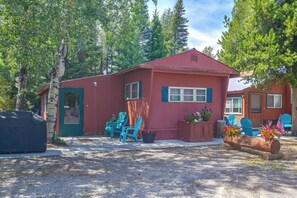 A red building with a porch, two blue chairs, and a wooden planter with flowers.