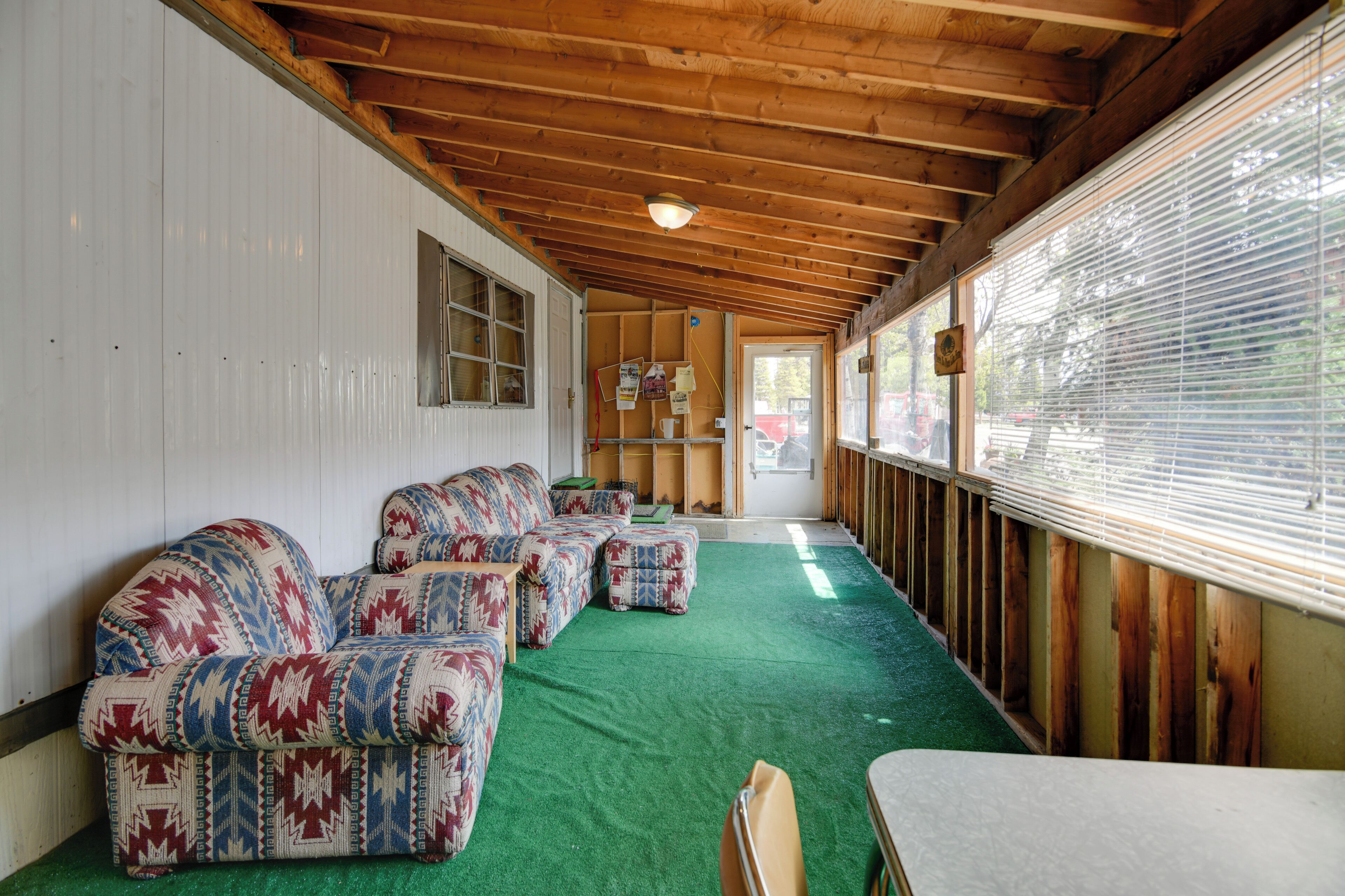 Un espace extérieur aménagé, abrité et doté d’une moquette verte, d’un plafond en bois et d’une vue à travers les stores.