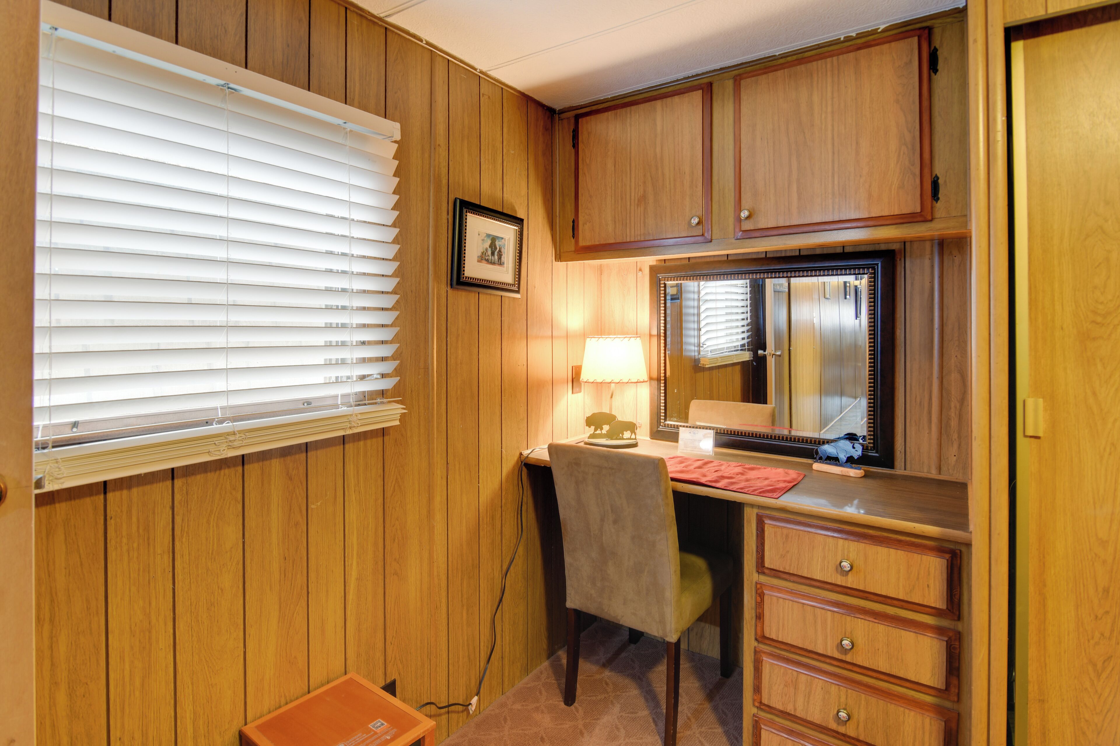 Una habitación con paneles de madera, un escritorio con silla, una lámpara, un espejo y un aparador.