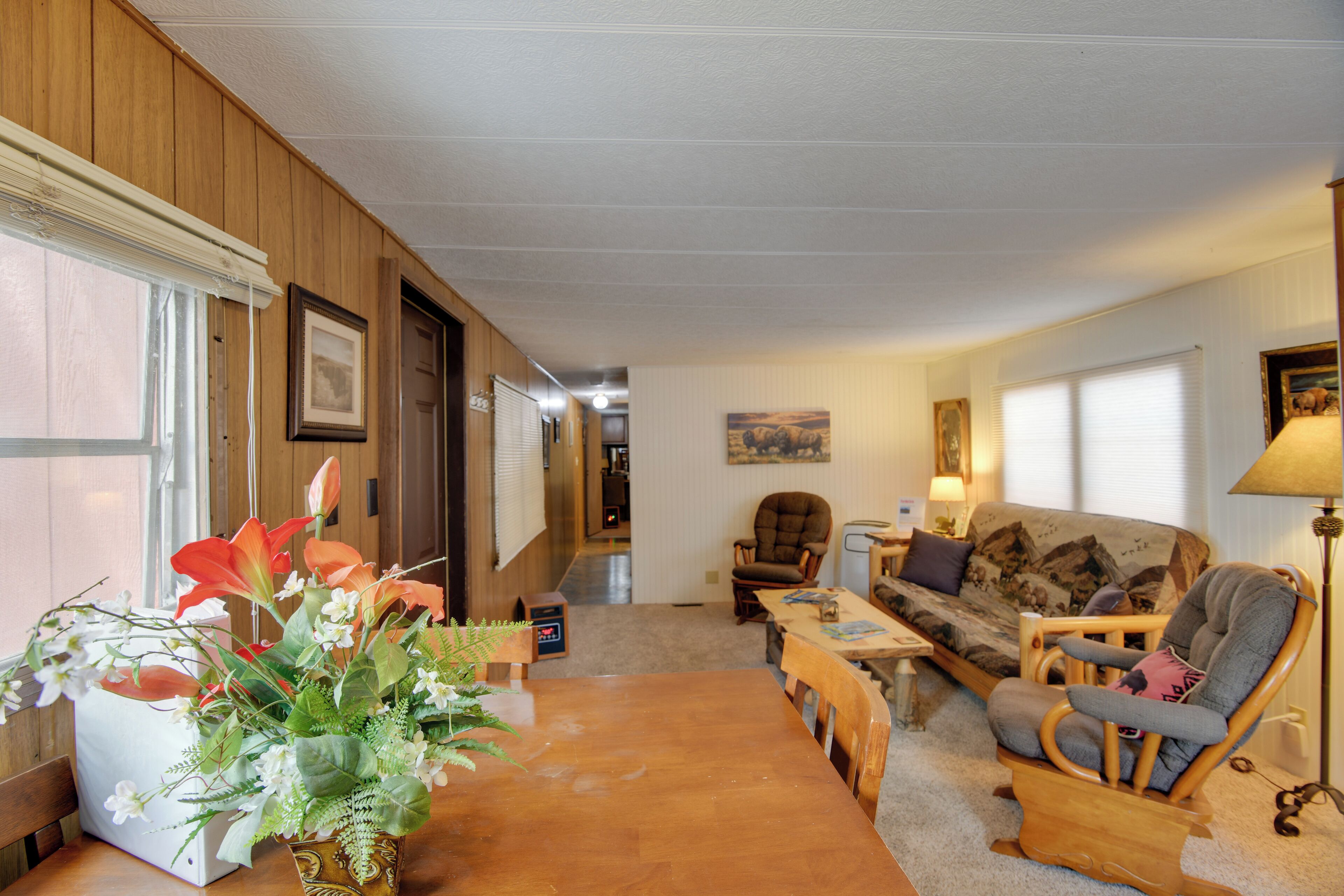 A living room with a wooden floor, a sofa, a rocking chair, a dining table, and a potted plant.