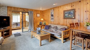 Um quarto com painéis de madeira, um sofá, uma mesa de centro, uma televisão e uma mesa de jantar com cadeiras.