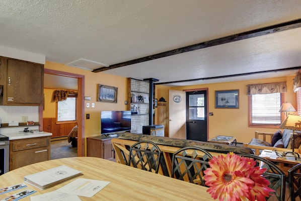 A kitchen with wooden cabinets, a dining table with chairs, a television, and a refrigerator. - Gateway to Yellowstone! Cabin < 1 Mi to Nat'l Park (West Yellowstone)