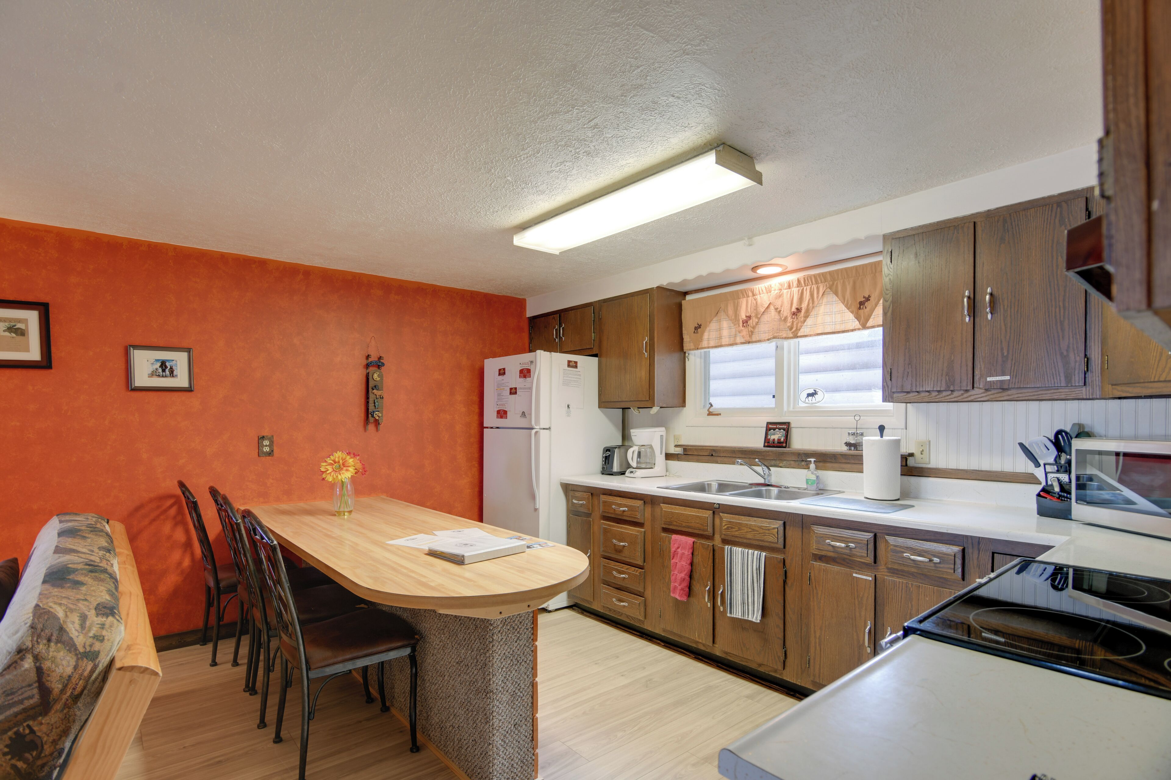 A compact kitchen with wooden cabinets, a dining area with chairs, a refrigerator, and a microwave.