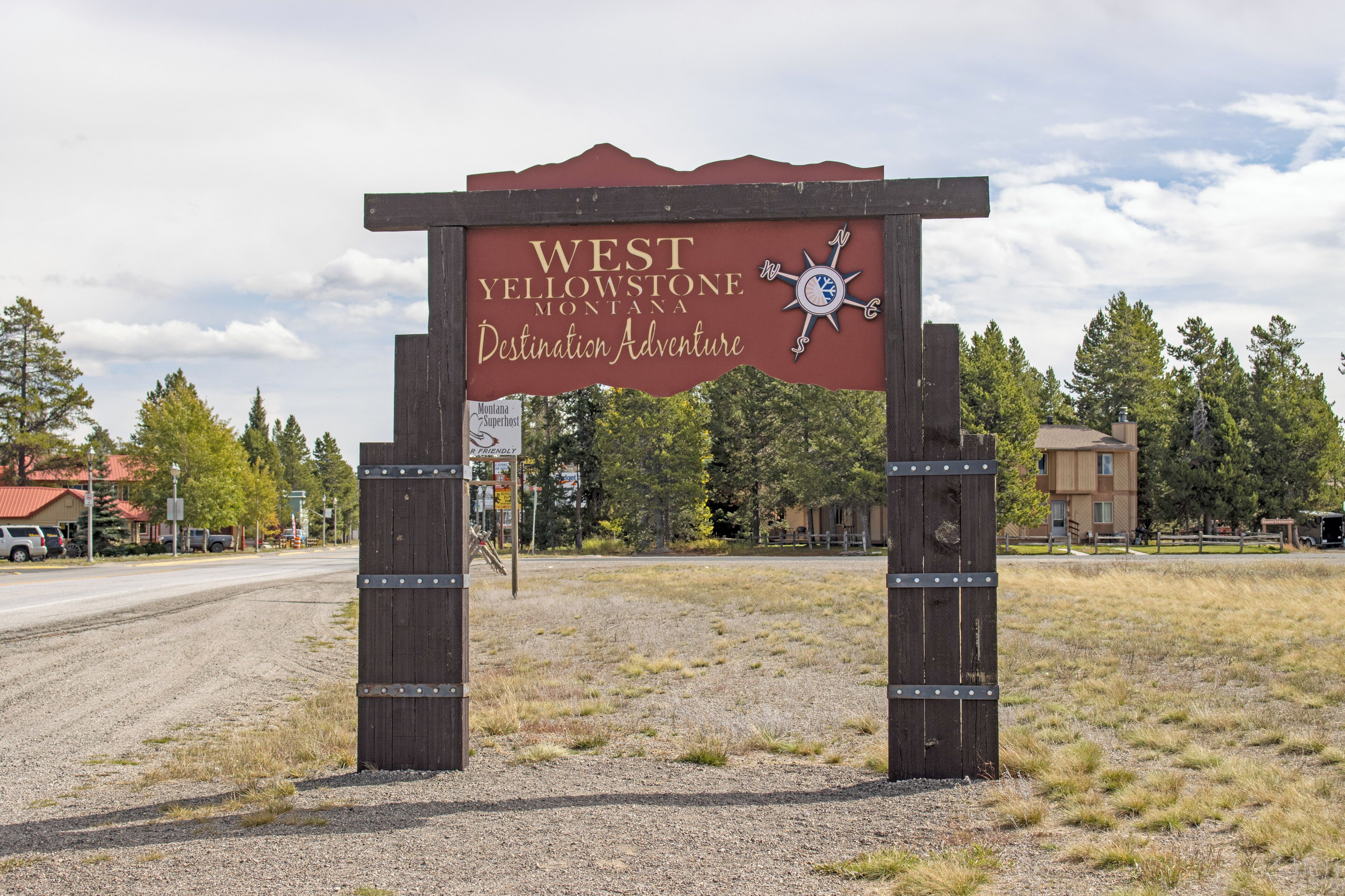 Un letrero de madera con el texto 'WEST YELLOWSTONE MONTANA Destination Adventure' y un símbolo de brújula.