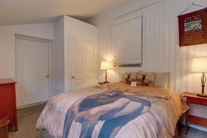 Ein Schlafzimmer mit einem Bett, zwei Nachttischen, einer Tür und einem Fenster mit Jalousien.