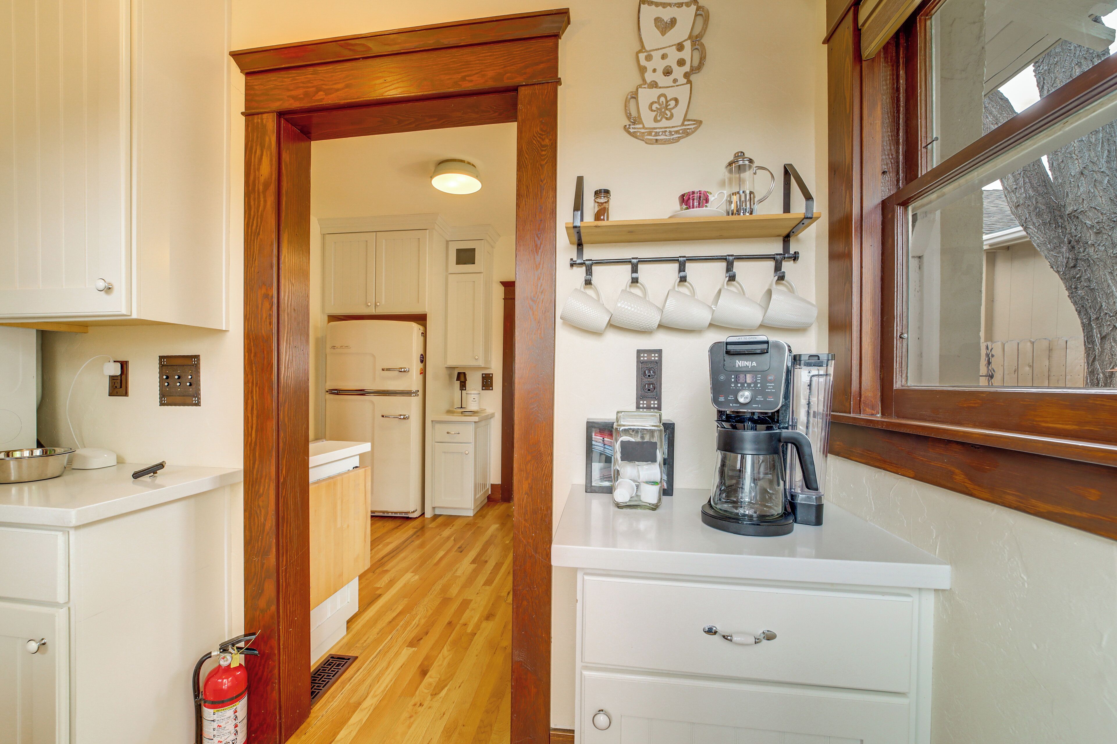 A kitchen with a coffee maker, a shelf with cups, and a fire extinguisher.
