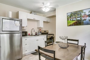 A kitchen with white cabinets, a stainless steel refrigerator, a microwave, and a gas stove. There is a dining table with chairs and a decorative metal centerpiece.