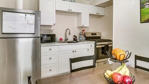 A modern kitchen with white cabinets, stainless steel appliances, a dining table with chairs, and a fruit bowl on the table.