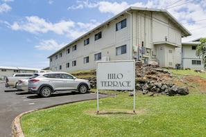 Un edificio con la leyenda 'HILO TERRACE', un estacionamiento y un área verde al frente.