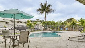 A pool area with lounge chairs, a table, and an umbrella.