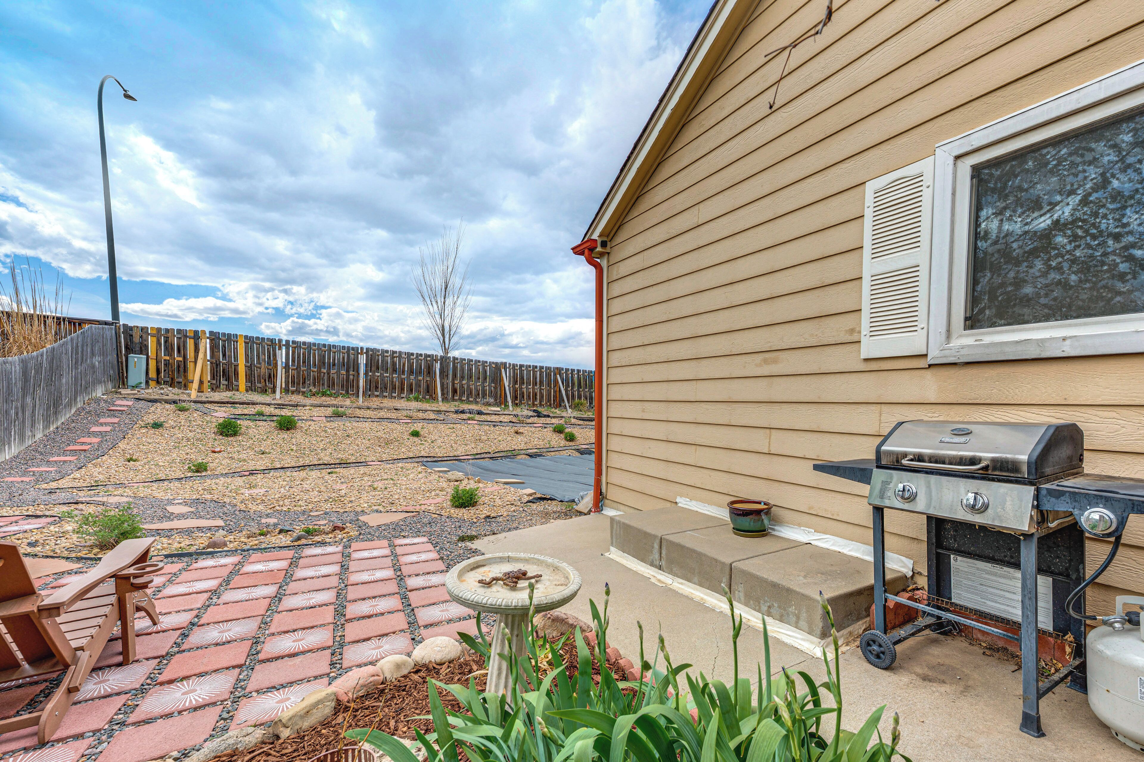 A backyard with a grill, a patio with a table and chairs, a wooden fence, and a house with siding.