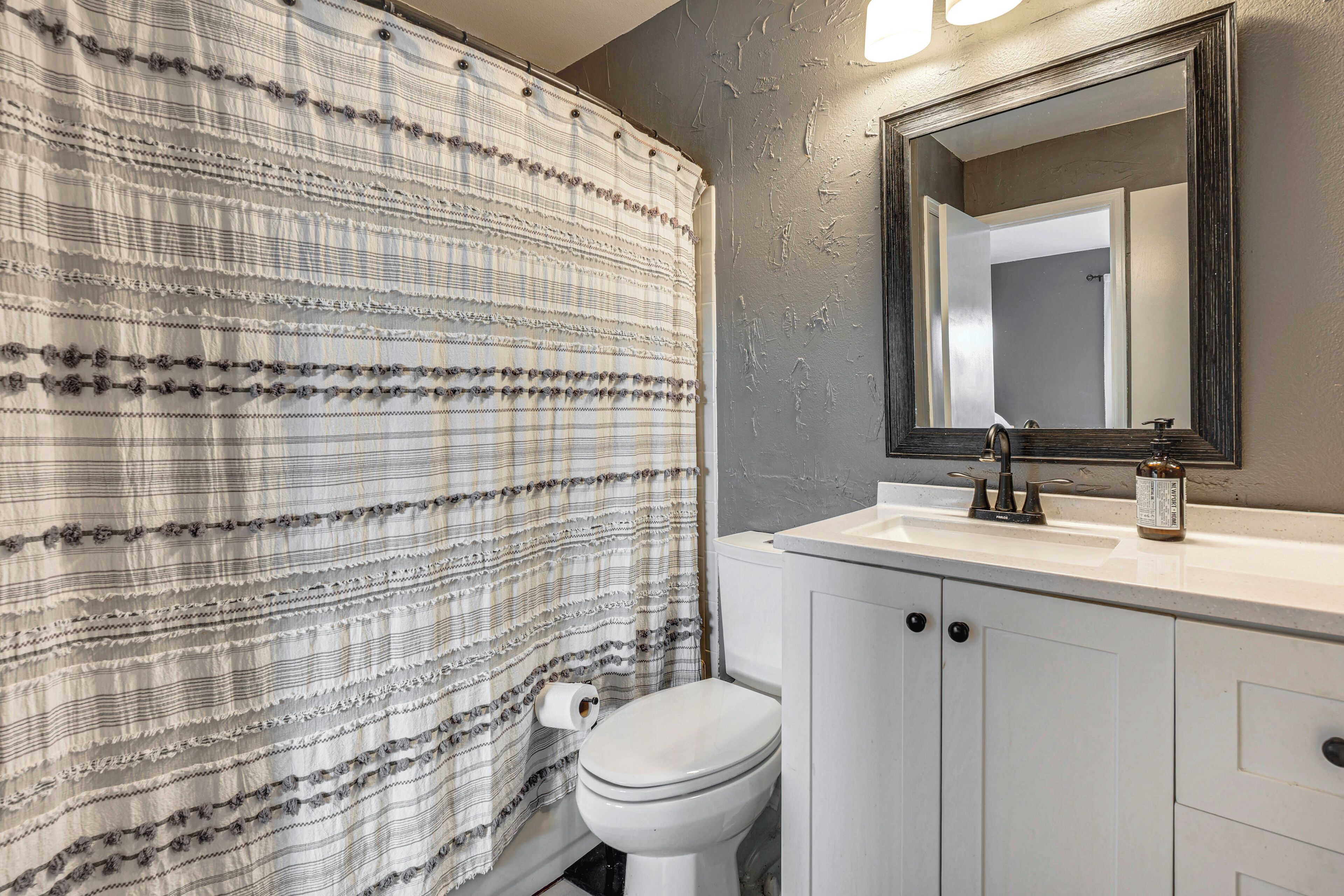 A bathroom with a striped shower curtain, a toilet, a sink with a mirror, and cabinets.