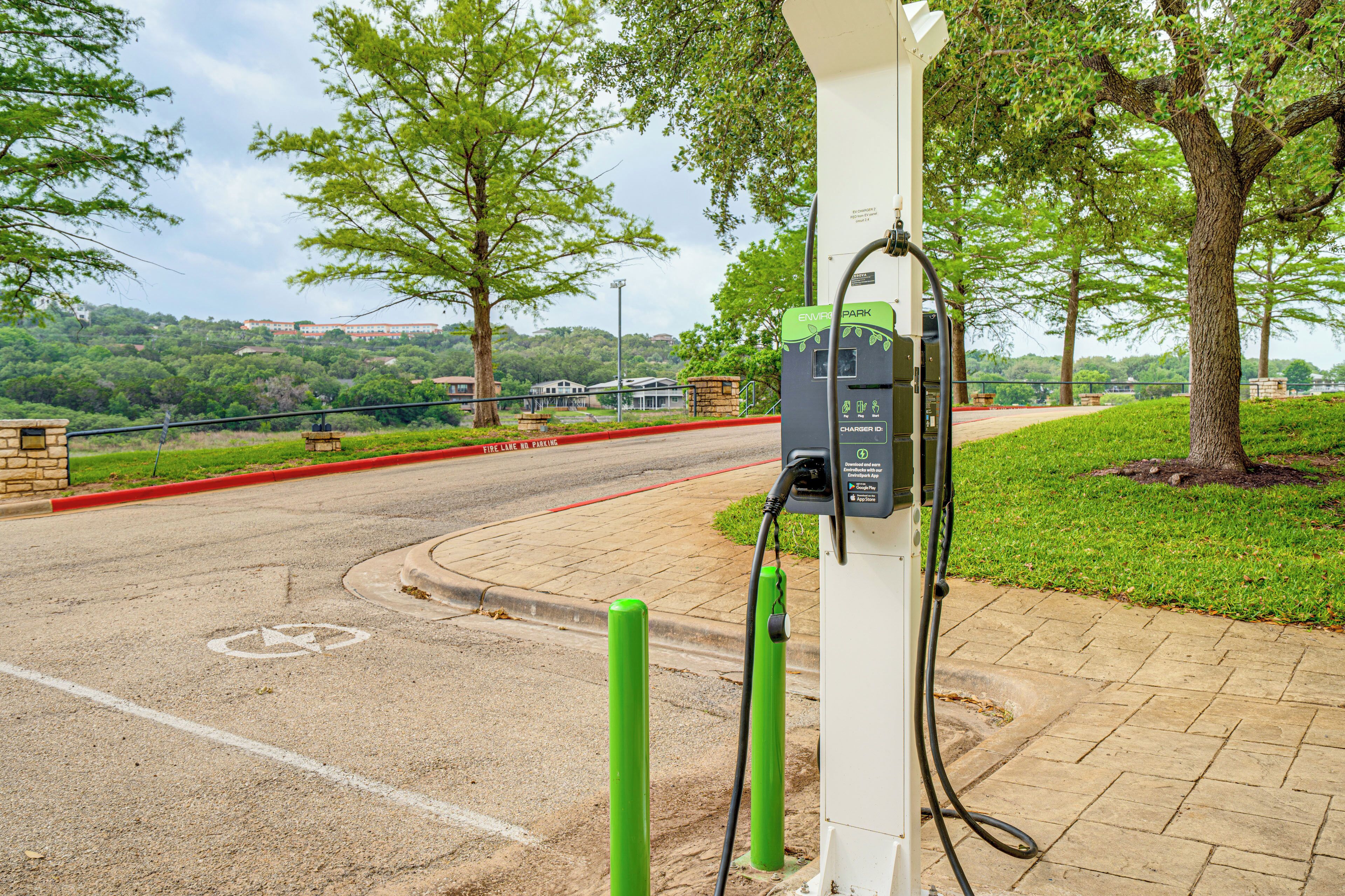 Estação de carregamento para veículos elétricos em área arborizada, com árvores e rua pavimentada.