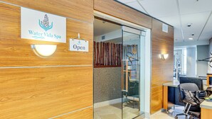 Ein Empfangsbereich mit einer Holzwand, einer Glastür und einem Schild, das anzeigt, dass der Spa geöffnet ist.