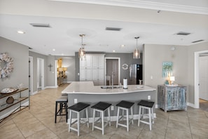 A modern kitchen with a central island, bar stools, pendant lighting, and a decorative wall piece. - Panoramic Stylish Gulf Retreat w/ Epic Pool Area (Panama City)