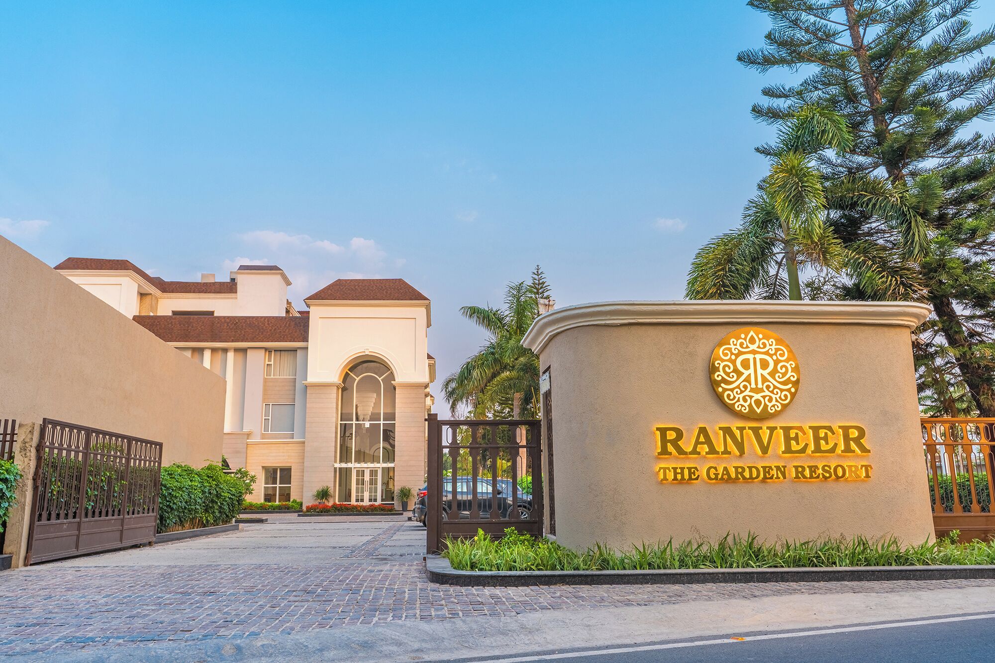 Una entrada con portón a Ranveer The Garden Resort bajo un cielo despejado.