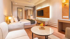 A hotel room with a bed, a seating area with a table, a television, and a mirror. - Ranveer the Garden Resort (Haldwani)