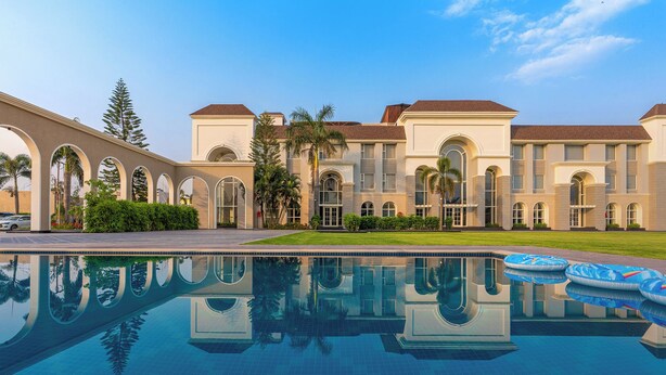 A large building with a swimming pool in front, featuring arched windows and a symmetrical facade. - Ranveer the Garden Resort (Haldwani)