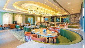 A modern restaurant with round tables, green and orange seating, and a central chandelier. - Ranveer the Garden Resort (Haldwani)