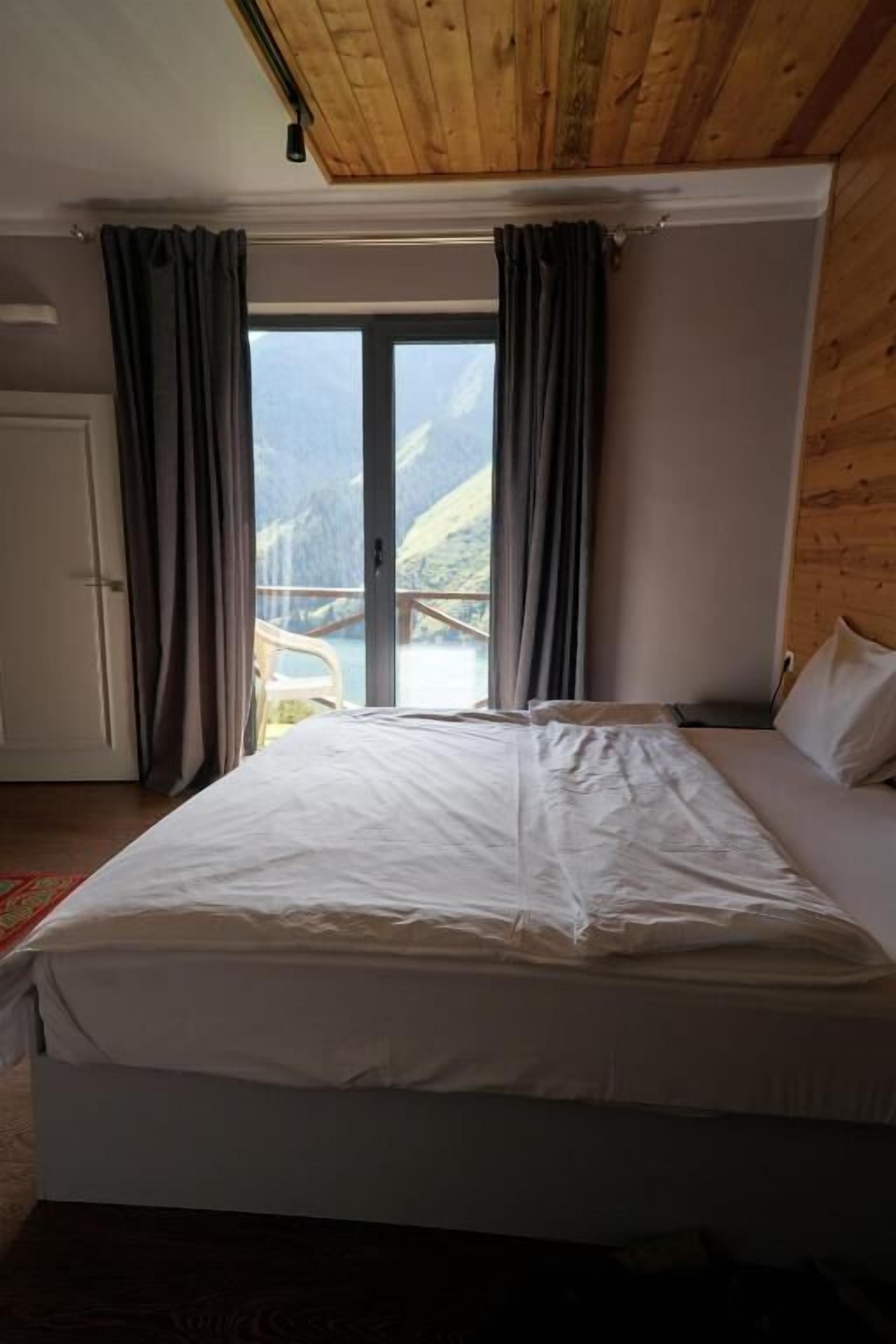 Ein Schlafzimmer mit Bett, Vorhängen, einer Schiebetür und Blick auf einen Berg.