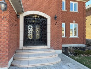 A brick house with a black ornate gate, white windows, and a small front yard with steps leading to the entrance.